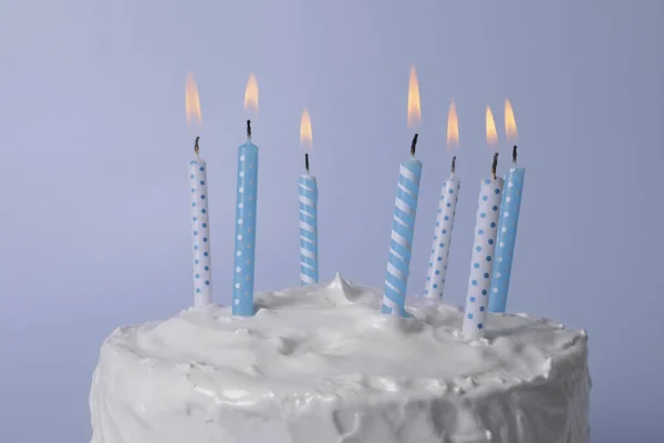 薄い青の背景にクリームと燃焼キャンドルとおいしいケーキ クローズアップ — ストック写真