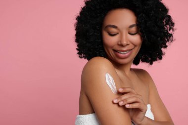 Genç bir kadın pembe arka planda vücut kremi sürüyor. Metin için boşluk