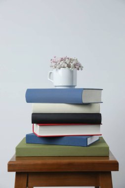 Hardcover kitapları ve beyaz duvarın yanındaki tahta taburede çiçekli fincan.