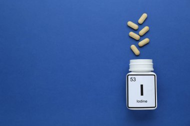 Mavi arka planda plastik kavanoz ve iyot hapları var. Metin için boşluk