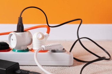 Kapalı alanda beyaz halının üzerinde farklı elektrik prizleri olan güç şeridi, yakın plan.