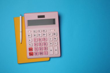 Açık mavi zemin üzerinde hesap makinesi, defter ve kalem, metin için boşluk ile düz yatar