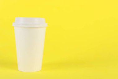 Sarı arka planda plastik kapaklı kağıt bardak, metin için boşluk. Kahve hazır.