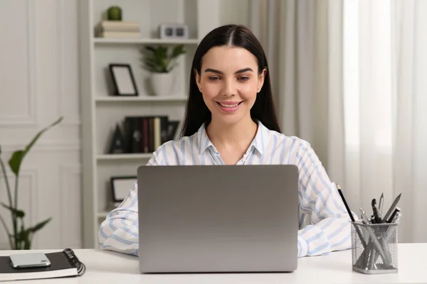 一个快乐的女人在房间的白色桌子边与笔记本电脑一起工作 — 图库照片