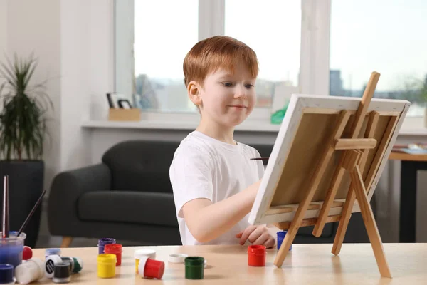 スタジオのテーブルで男の子が絵を描く キャンバスを保持するためにイーゼルを使用 — ストック写真