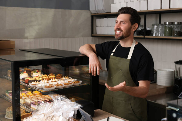 Portrait of happy seller at cashier desk in bakery shop