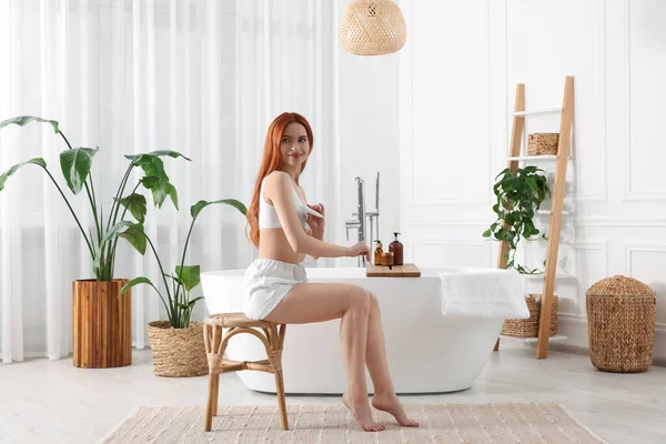 stock image Beautiful young woman applying body cream onto arms in bathroom, space for text