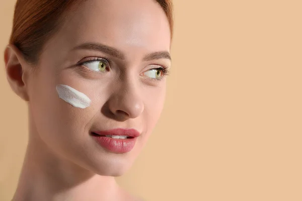 Beautiful young woman with sun protection cream on her face against beige background, closeup. Space for text