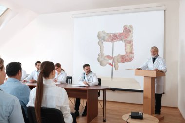 Gastroenteroloji dersi. Profesör ve doktorlarla dolu bir konferans odası. Kalın bağırsak resimli projeksiyon ekranı