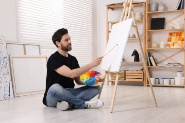 Stüdyoda resim yapan adam. Tuvali tutmak için resim sehpası kullanılıyor