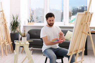 Stüdyoda resim yapan adam. Tuvali tutmak için resim sehpası kullanılıyor