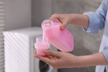 Kadın iç çamaşırları yıkamak için şişeden kapağa kumaş yumuşatıcısı döküyor.