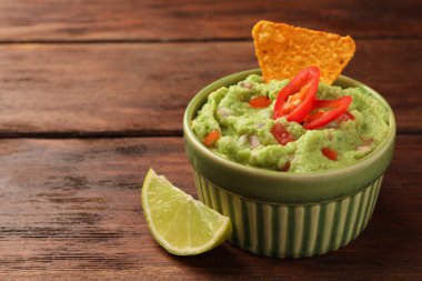 Bir kase lezzetli guacamole, cips ve limonlu ahşap masa, yakın plan. Metin için boşluk