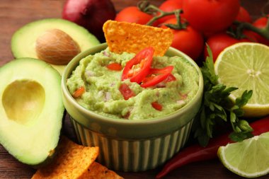 Bir kase lezzetli guacamole, cips ve ahşap masa malzemeleri, yakın plan.