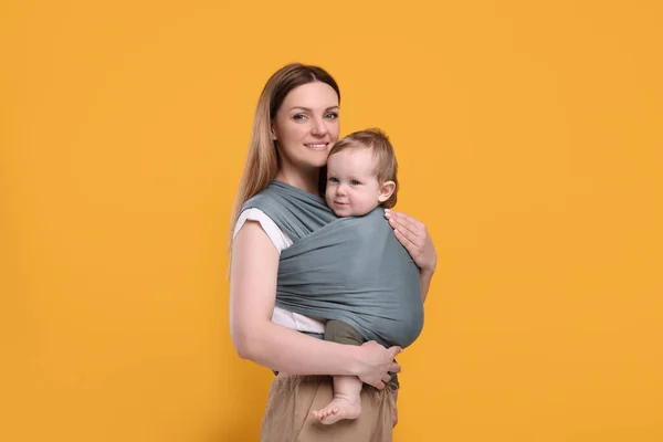 stock image Mother holding her child in baby wrap on orange background