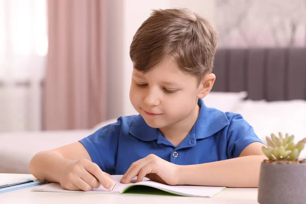Kleiner Junge Löscht Fehler Seinem Notizbuch Weißen Schreibtisch Drinnen — Stockfoto