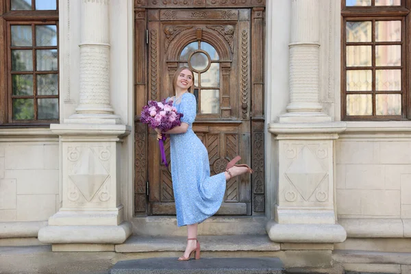 stock image Beautiful woman with bouquet of spring flowers near building outdoors