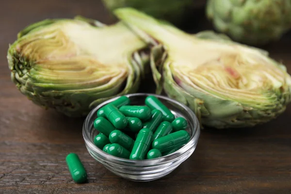 stock image Bowl with pills and fresh artichokes on wooden table, closeup