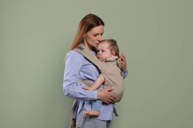 Anne zeytin arka planında çocuğunu askıda (bebek taşıyıcısı) tutuyor