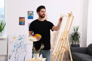 Stüdyoda resim yapan adam. Tuvali tutmak için resim sehpası kullanılıyor