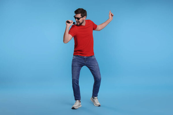 Handsome man with sunglasses and microphone singing on light blue background