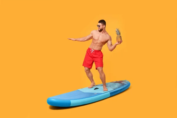 stock image Man with pineapple posing on SUP board against orange background