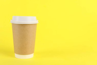 Sarı arka planda plastik kapaklı kağıt bardak, metin için boşluk. Kahve hazır.
