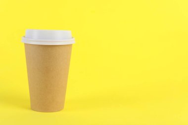 Sarı arka planda plastik kapaklı kağıt bardak, metin için boşluk. Kahve hazır.