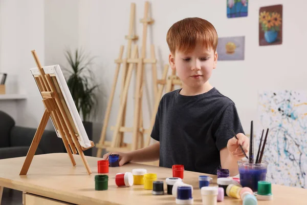 スタジオのテーブルで男の子が絵を描く キャンバスを保持するためにイーゼルを使用 — ストック写真