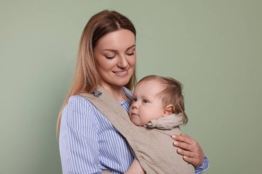 Anne zeytin arka planında çocuğunu askıda (bebek taşıyıcısı) tutuyor