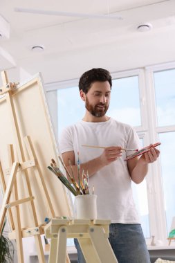 Stüdyoda resim yapan adam. Tuvali tutmak için resim sehpası kullanılıyor