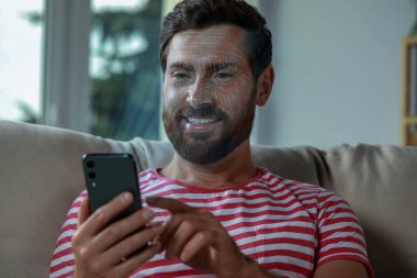 Evde yüz tanıma sistemi olan akıllı telefon kullanan bir adam. Güvenlik başvurusu sahibinin kimliğini doğrulamak için yüzünü tarıyor.