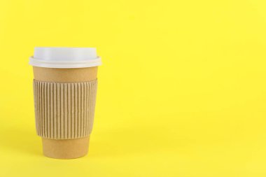 Sarı arka planda plastik kapaklı kağıt bardak, metin için boşluk. Kahve hazır.