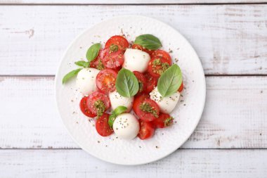 Domatesli Caprese salatası, mozzarella topları ve beyaz ahşap masada fesleğen.