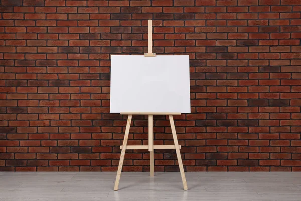 stock image Wooden easel with blank canvas near brick wall indoors