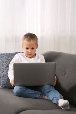 Evdeki kanepede dizüstü bilgisayar kullanan küçük bir kız. İnternet bağımlılığı