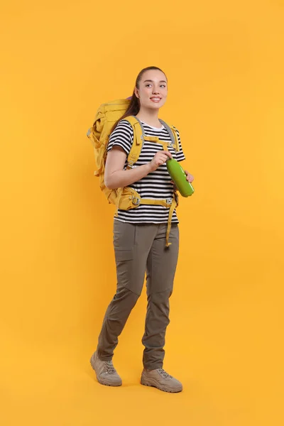 Leende Ung Kvinna Med Ryggsäck Och Termoflaska Orange Bakgrund Aktiv — Stockfoto
