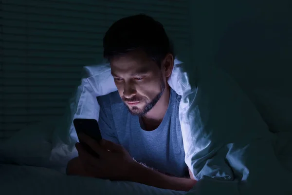 Man using smartphone under blanket in bed at night. Internet addiction