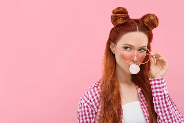 Stock image Beautiful woman with bright makeup blowing bubble gum on pink background. Space for text