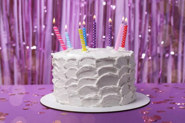 紫の背景にクリームと燃焼キャンドルとおいしいケーキ — ストック写真