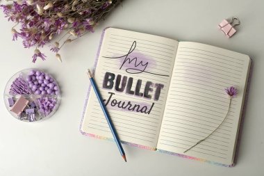 Verimliliğini arttır. Sözcüklerle dolu bir defter. Kurşun günlüğüm, kırtasiyem ve çiçeklerim beyaz masanın üstünde.