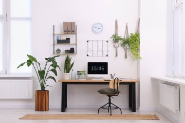 Bilgisayarlı, modern mobilyalı ve evdeki ev bitkileriyle rahat bir iş yeri.