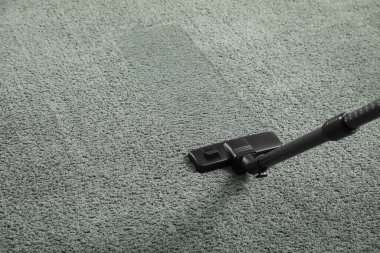 Gri halıdaki toprağı modern elektrik süpürgesiyle temizliyorum. Metin için boşluk