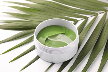 Beyaz arka planda kaşık ve palmiye yapraklı kavanoz dolusu göz bandı, yakın plan. Kozmetik ürünü