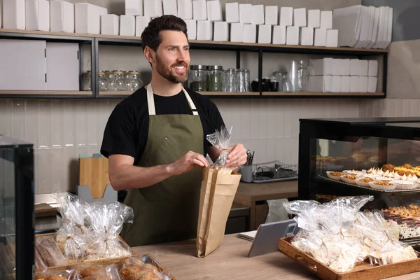 stock image Happy seller putting pastry into paper bag at cashier desk in bakery shop