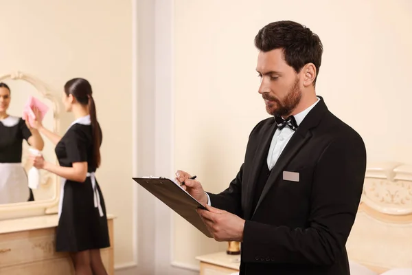 穿着西服的男人穿着剪贴板检查女佣在酒店房间里的工作 文字空间 专业管家课程 — 图库照片