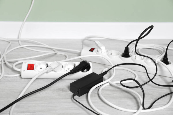 Power strips with different electrical plugs on white floor indoors, closeup