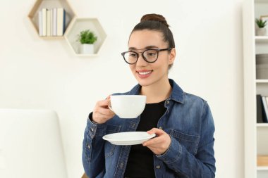 Ev işyerinde. Bir fincan sıcak içecekle odada dizüstü bilgisayara bakan mutlu bir kadın.