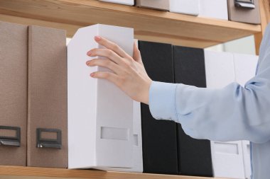 Woman taking folder with documents from shelf in office, closeup