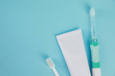 Elektrikli diş fırçaları ve açık mavi arka planda diş macunu. Metin için boşluk